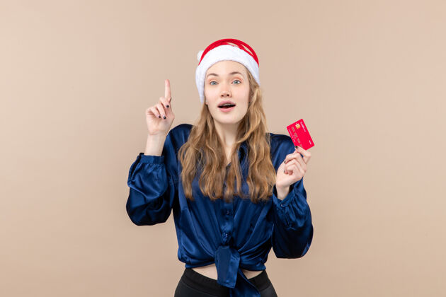 人正面图年轻女性手持红色银行卡在粉色背景上的圣诞钱照片节日新年感慨钱年轻银行