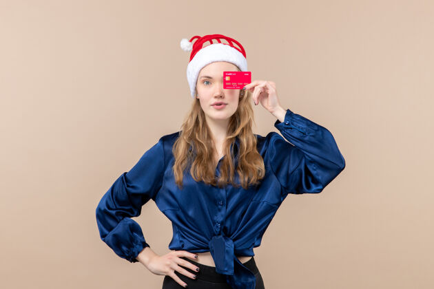 帽子正面图年轻女性手持红色银行卡 背景为粉色节日圣诞钱照片新年感慨年轻的女性年轻人