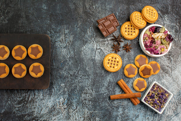 景观木制盘子上的饼干 巧克力条和灰色地面上的干花碗的俯视图顶部地面碗
