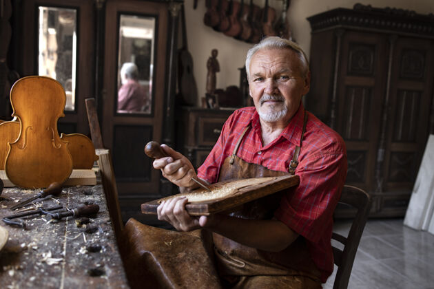 压花老木匠拿着工具和木头在他的旧时装工作室的画像硬木技能木材