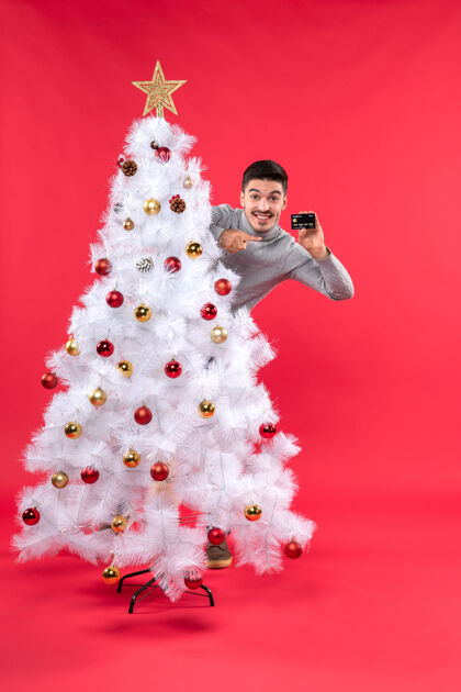 快乐圣诞节心情与情绪化的家伙站在装饰圣诞树后 并采取电话婚礼电话礼服