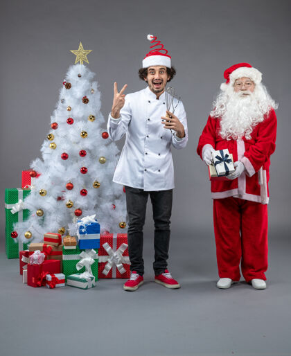 服装圣诞老人和男厨师在灰色墙上围着圣诞礼物的正视图厨师十二月正面