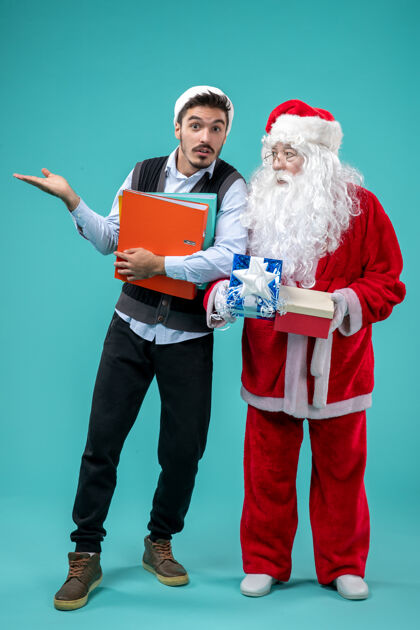 蓝色前视图圣诞老人与年轻的男性和礼物上的蓝色背景男人圣诞老人成人
