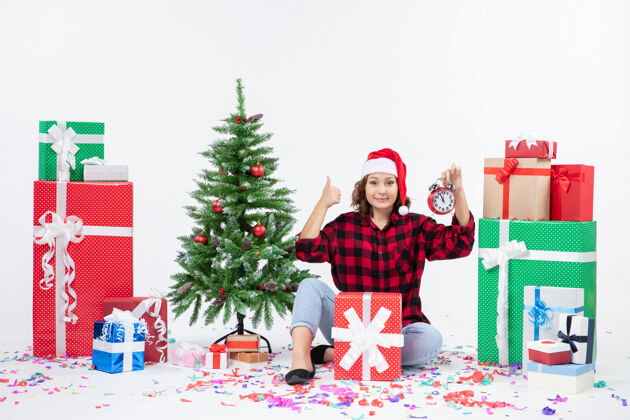 快乐前视图的年轻女子坐在圣诞礼物周围拿着白色墙上的时钟礼物礼物节日