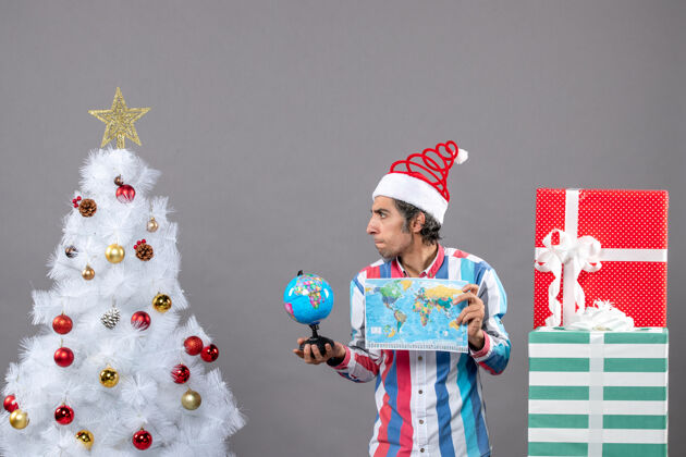 地球前视图好奇的男子与螺旋弹簧圣诞帽举行世界地图和地球仪礼品盒假期盒子