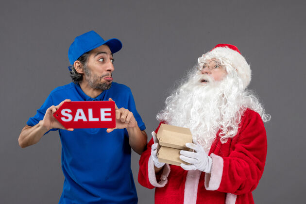 举行圣诞老人的正面图 男信使手持销售横幅 灰色墙上有食品包装帽子快乐圣诞老人