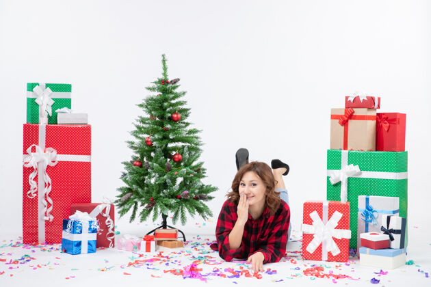 铺设正面图：年轻女性躺在白色背景上的圣诞礼物和圣诞树上 圣诞礼物的颜色是雪白的圣诞礼物年轻人