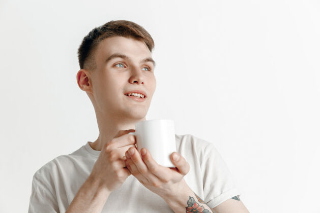 杯子喝咖啡休息英俊的年轻人拿着咖啡杯 微笑着站在灰色的工作室背景下优雅相机人