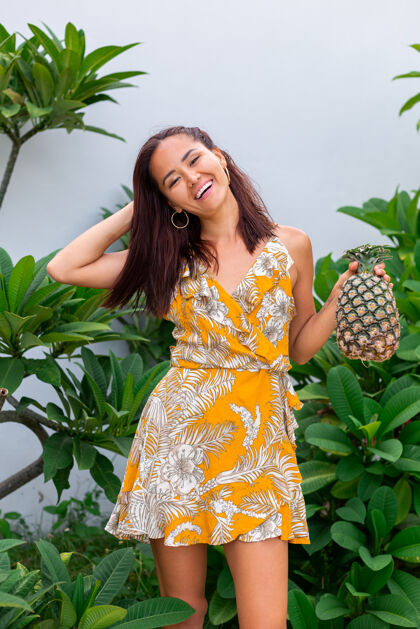 举行身着黄色夏装 手持菠萝的快乐亚洲微笑女人的画像饮食美丽绿色