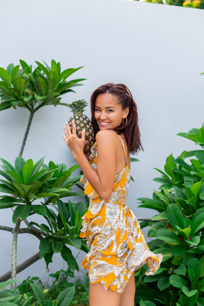 女人身着黄色夏装 手持菠萝的快乐亚洲微笑女人的画像夏天绿色自然