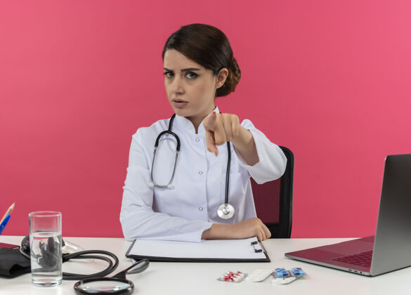 医疗严格的年轻女医生 穿着医用长袍 带听诊器 坐在办公桌旁 用医疗工具在电脑上显示你的手势和复印空间长袍手势听诊器