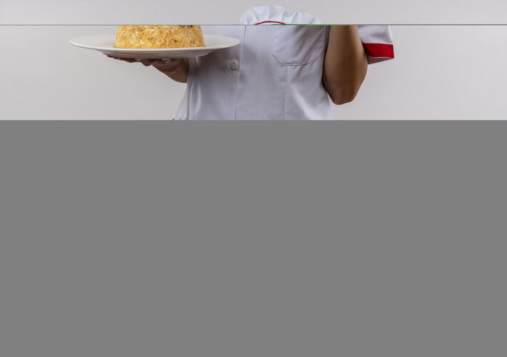 年轻高兴的年轻厨师女穿着厨师制服拿着蛋糕盘上她的大拇指在孤立的白色墙壁与复制空间制服盘子拿着