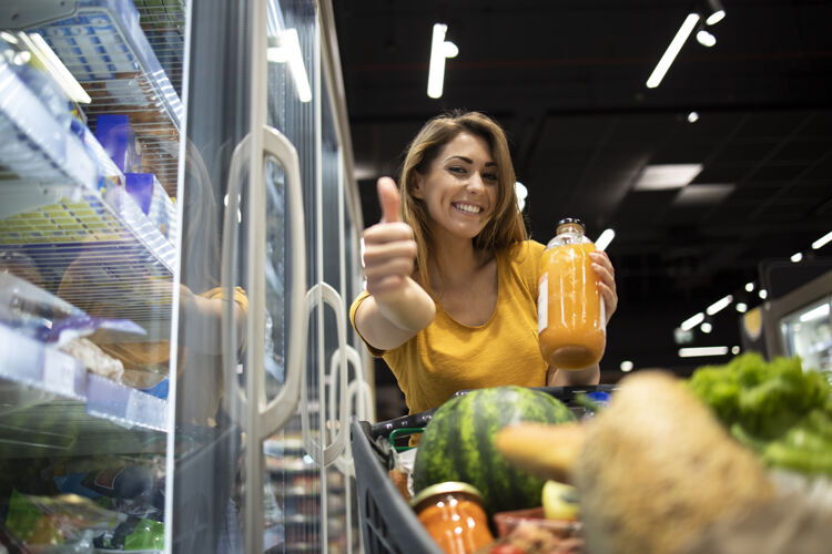销售在杂货店拿着橙汁竖起大拇指的女人竖起大拇指阅读货架