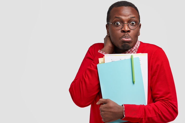 眼镜迷茫的黑人困惑地看着 拿着纸和笔 穿着红色的套头衫民族毛衣困惑
