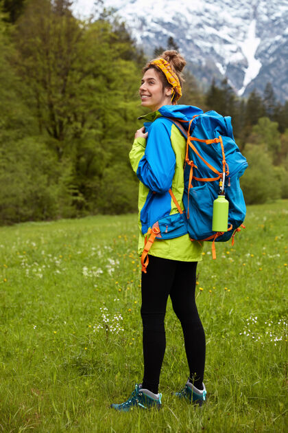 登山穿着运动服 漫步在绿色草地上的快乐的活动女游客的垂直全长镜头风景活跃背包