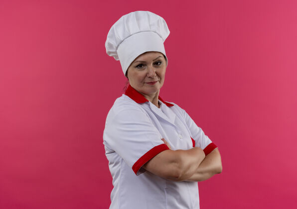 交叉身着厨师制服的中年女厨师双手交叉放在隔离的粉色墙壁上 留有临摹空间制服手厨师