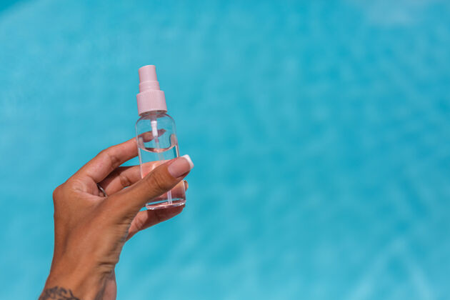 护肤手拿着一小瓶晒黑油液在蓝色的游泳池上方热带举行女人