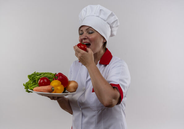 封闭闭着眼睛 身着厨师制服的中年女厨师拿着盘子里的蔬菜 用拷贝空间咬掉西红柿中年厨师蔬菜