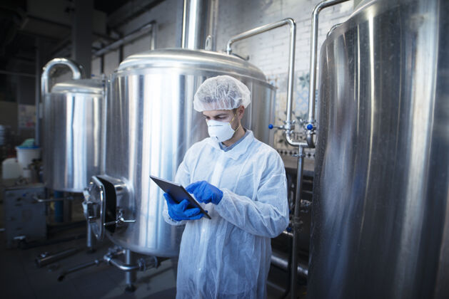 专业一位经验丰富的技术人员 穿着白色防护服 手持药片 在加工厂控制食品生产设备轨道记录