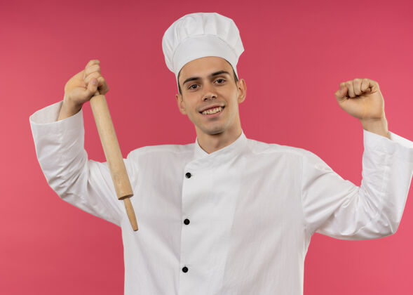 厨师微笑的年轻男厨师身穿厨师制服手持擀面杖做着坚强的手势别针戴着男性
