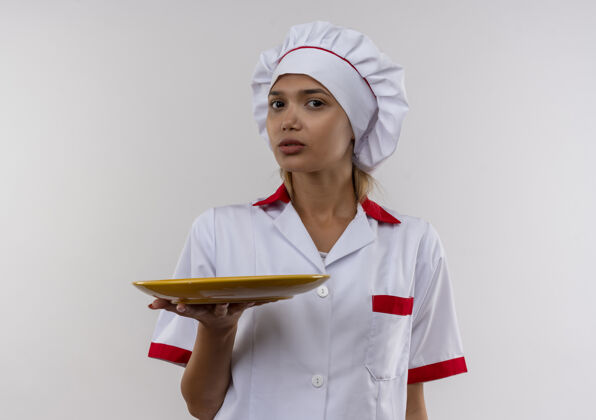 女年轻的女厨师穿着厨师制服拿着盘子在隔离的白色墙上留着复印空间看着戴着厨师