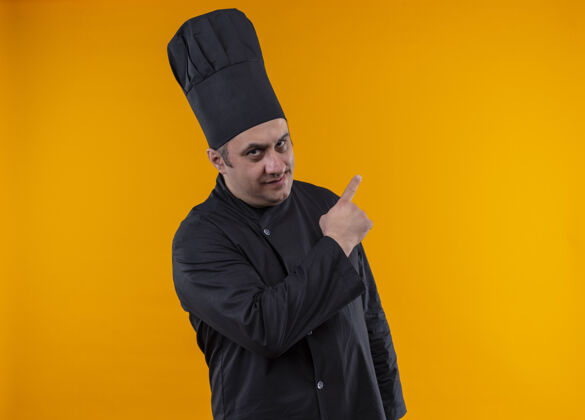 制服自信的中年男厨师身着厨师制服 指着黄色墙壁的侧面 留有临摹空间分厨师中年