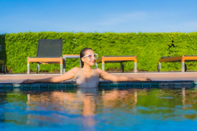 游泳美丽的亚洲年轻女子在度假酒店的室外游泳池周围放松的肖像享受放松健康