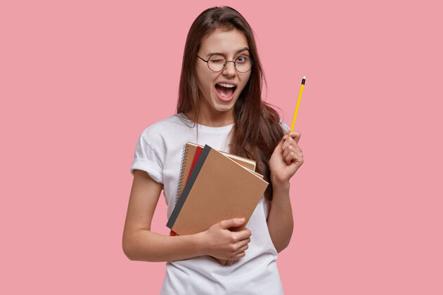 散文快乐年轻的白种女天才得到好主意 眨眼 拿铅笔 拿笔记本 在室内玩T恤创新考试