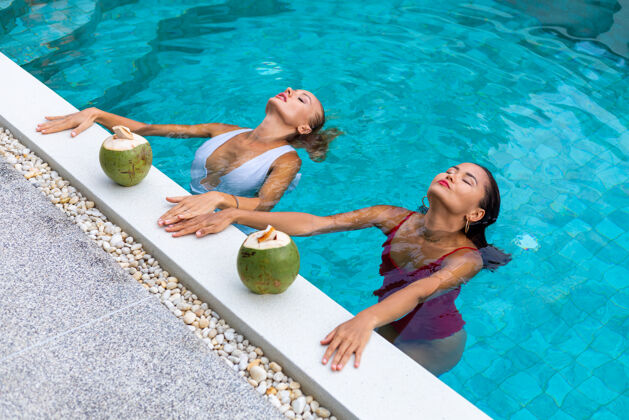 度假村两位亚洲人和白种人的女性朋友在别墅的游泳池化妆酒店比基尼饮料