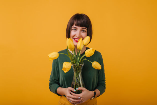 黄色一幅室内肖像画 一头黑发 穿着绿色毛衣 手里拿着一瓶漂亮的花一位心醉神迷的短发女士站在郁金香旁边表情植物黄色花