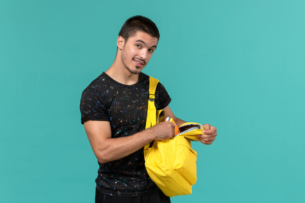 成人浅蓝色墙壁上穿着深色t恤黄色背包的男学生正面图模特大学大学