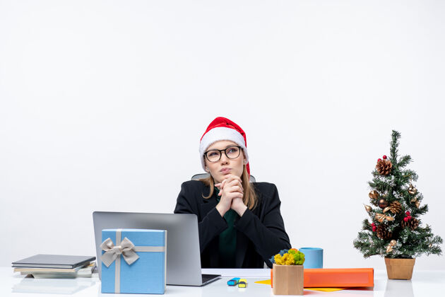 圣诞老人在办公室里 一位体贴迷人的女士戴着圣诞帽坐在一张桌子旁 桌上放着圣诞树和一份礼物圣诞树帽子公司