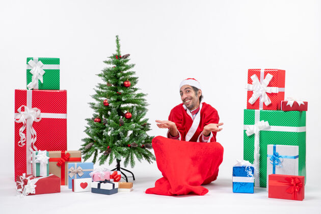 年轻人笑容满面的年轻人坐在地上庆祝新年或圣诞节 旁边有礼物和装饰圣诞树礼物地圣诞树