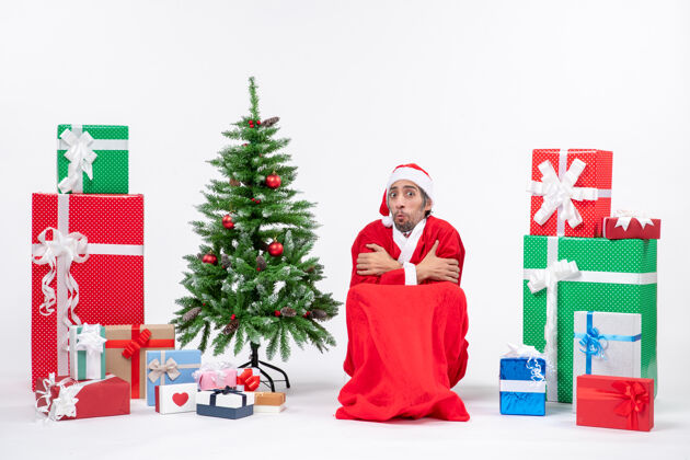 年轻人冰冻的年轻人打扮成圣诞老人与礼物和装饰圣诞树上的白色背景人年轻人礼物