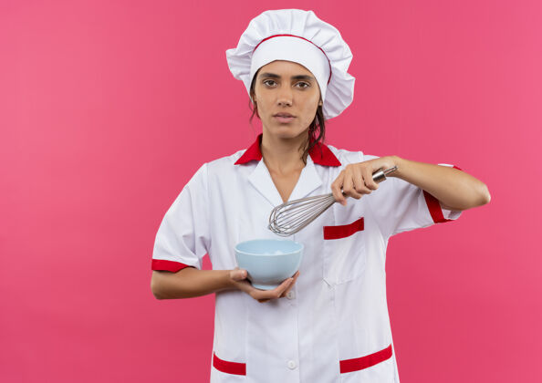 厨师年轻的女厨师穿着厨师制服 拿着碗 在隔离的粉色墙壁上打招呼 还有复印空间碗看年轻