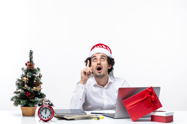 礼物快乐积极的年轻商人 戴着滑稽的圣诞老人帽 在白色背景的办公室里向上看圣诞节人圣诞老人