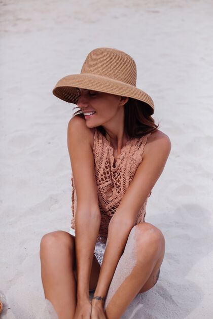 快乐年轻漂亮的白种人 皮肤黝黑 穿着针织衣服 戴着帽子在沙滩上天然上衣手提包